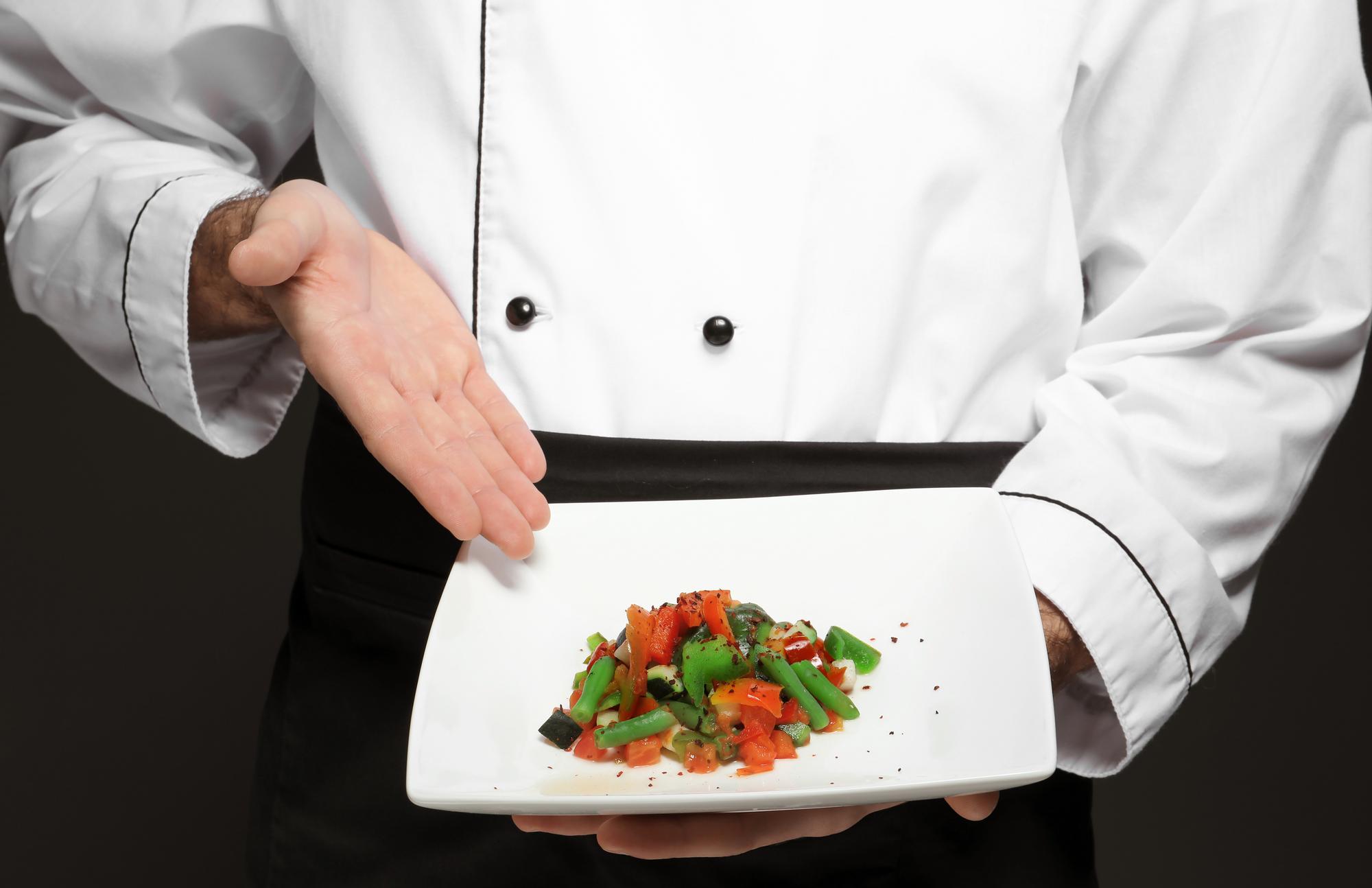 Chef demonstrating plated gourmet dish in a refined kitchen